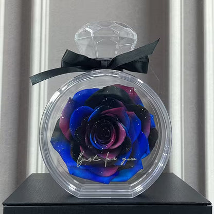 Blue and pink rose in a clear container with a black bow on a gray surface.