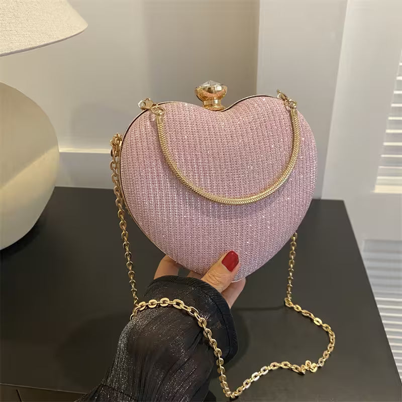 Heart-shaped pink handbag with gold chain held by a person on a dark surface.