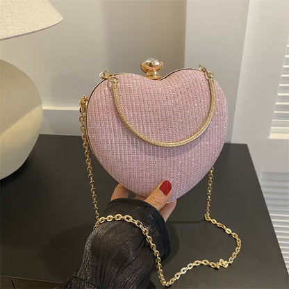Heart-shaped pink handbag with gold chain held by a person on a dark surface.
