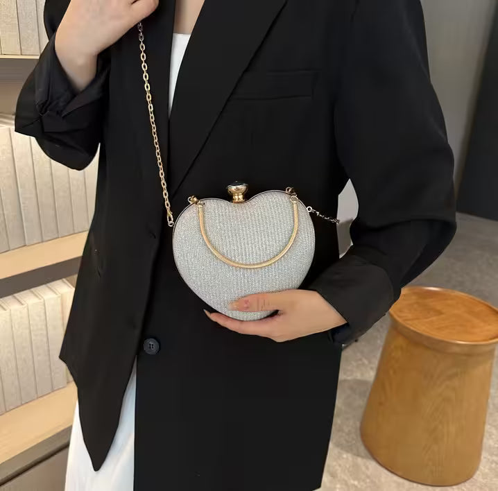 Person holding a heart-shaped clutch bag with a gold chain in an indoor setting