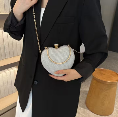 Person holding a heart-shaped clutch bag with a gold chain in an indoor setting