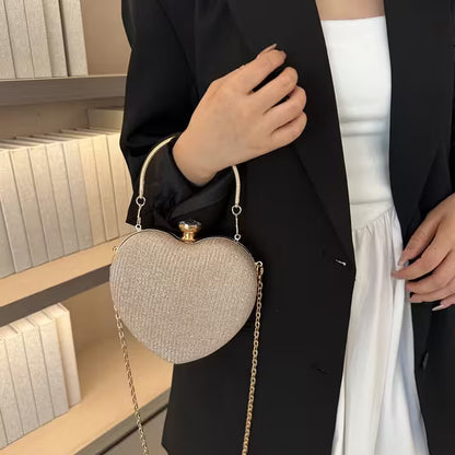 Heart-shaped handbag held by a person in a black coat and white skirt against a bookshelf background