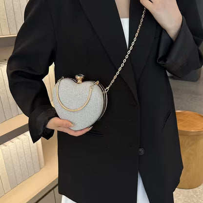 Person holding a heart-shaped clutch bag with a gold chain in an indoor setting