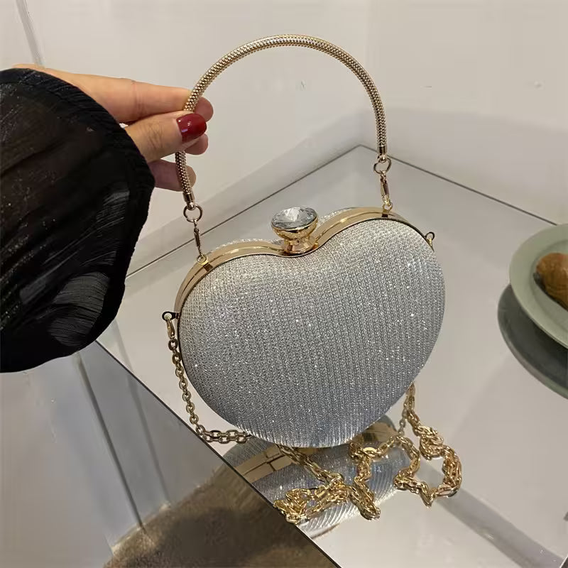 Heart-shaped handbag with gold chain and handle held by a person.