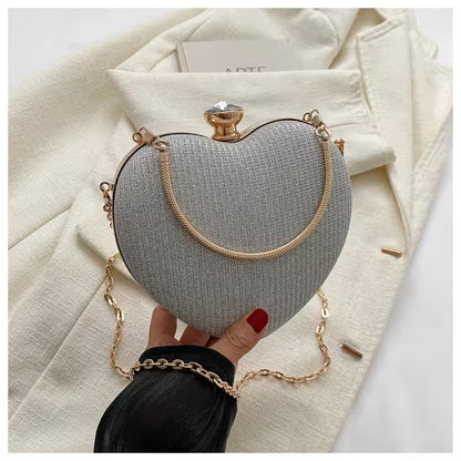Heart-shaped clutch bag with gold chain held by a hand against a white background