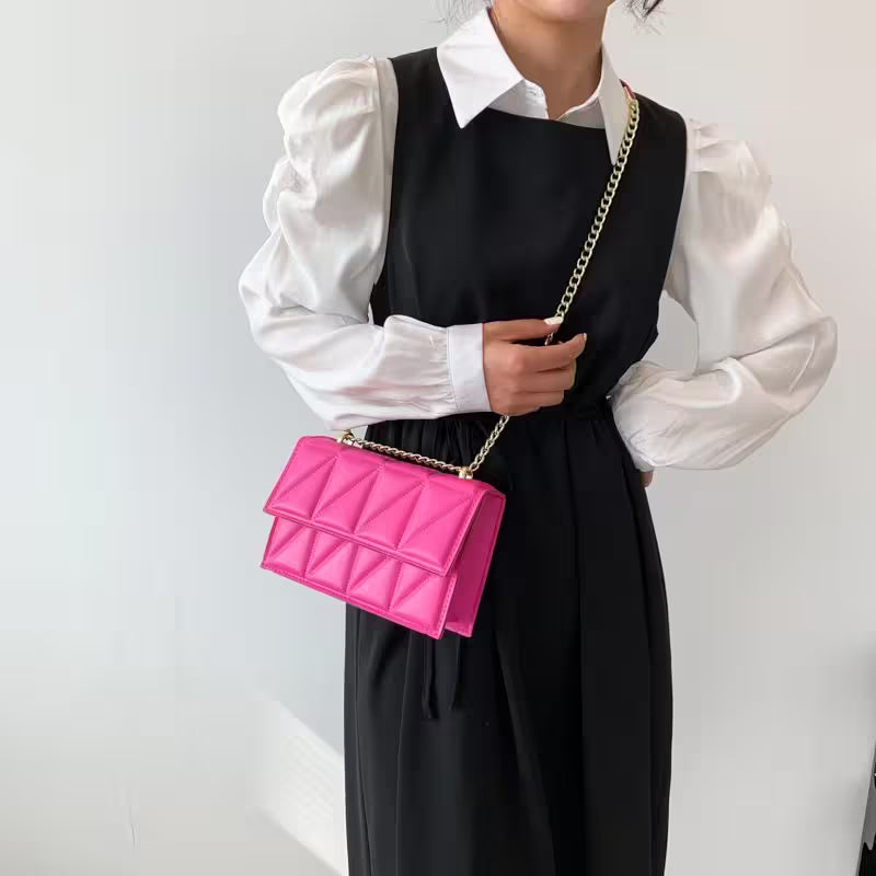 Person wearing a black dress over a white shirt, holding a pink quilted handbag with a gold chain strap.