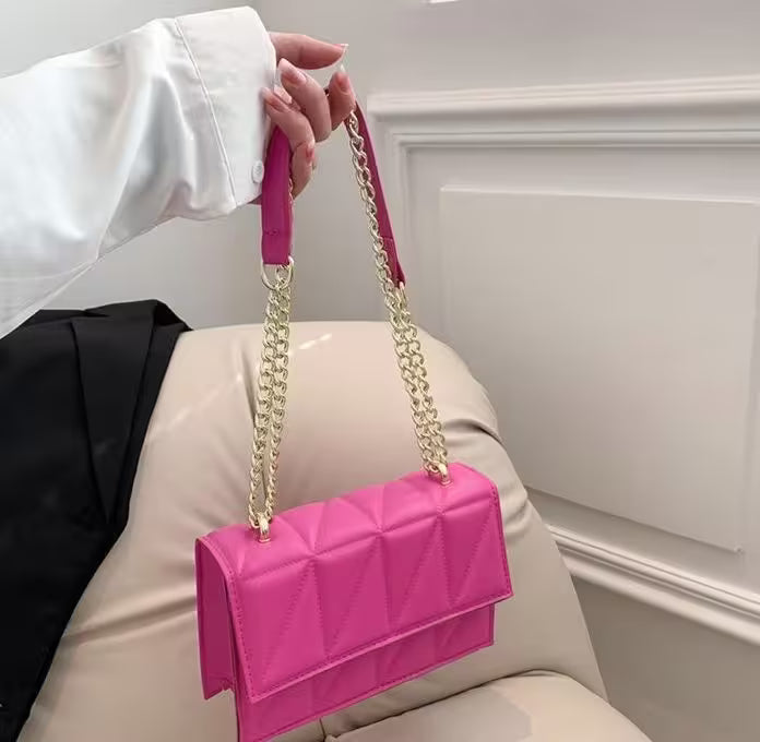 Person holding a pink handbag with a gold chain strap against a neutral background