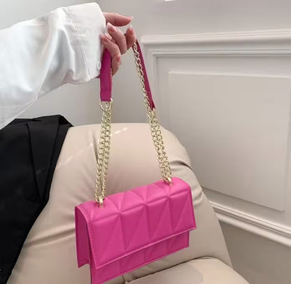 Person holding a pink handbag with a gold chain strap against a neutral background