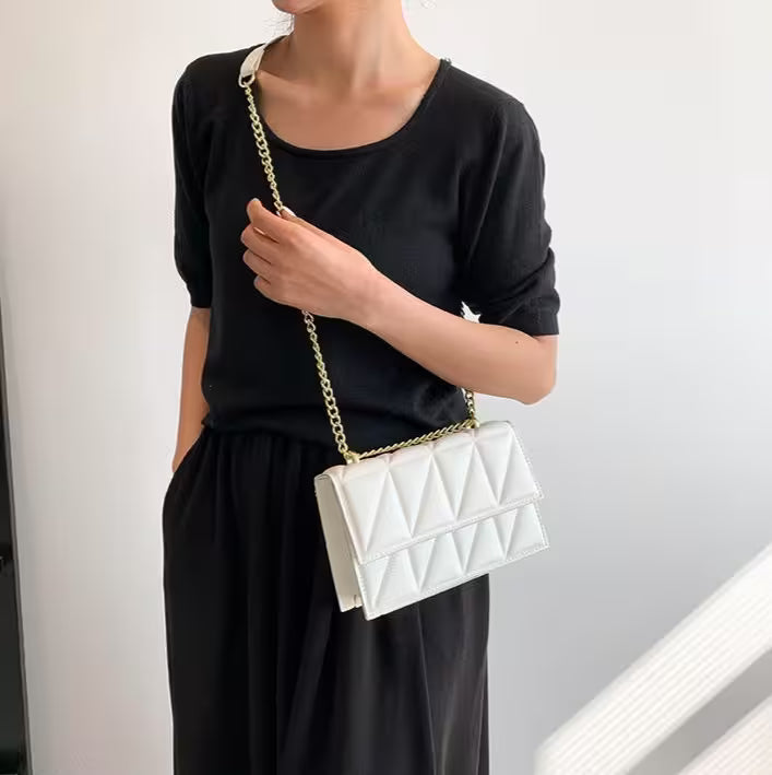 Person holding a white quilted handbag with a gold chain strap against a neutral background