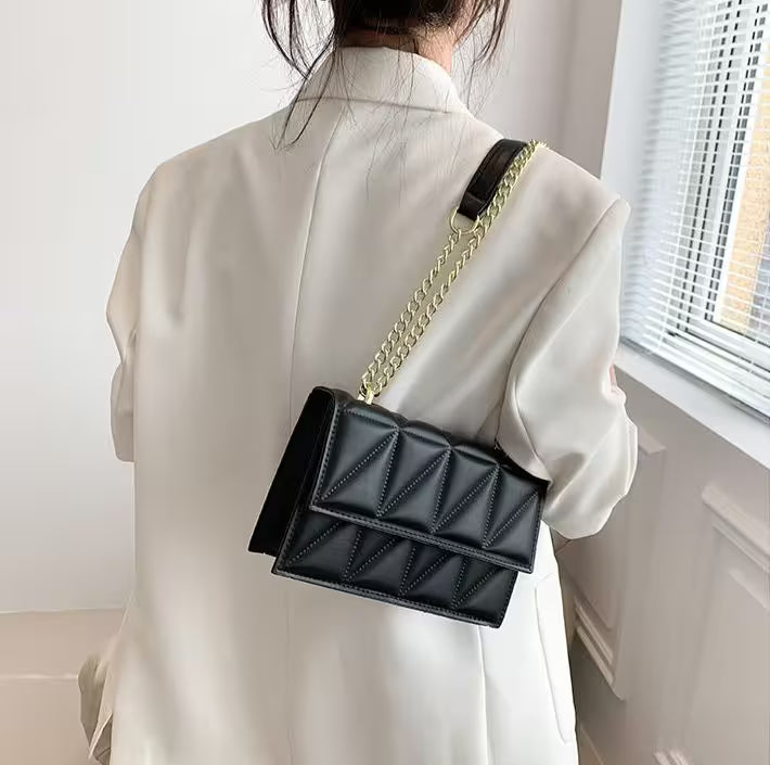 Person wearing a black quilted handbag with a gold chain strap indoors.