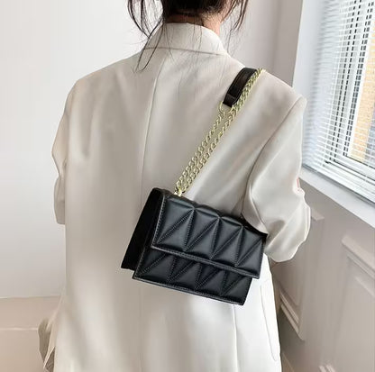 Person wearing a black quilted handbag with a gold chain strap indoors.
