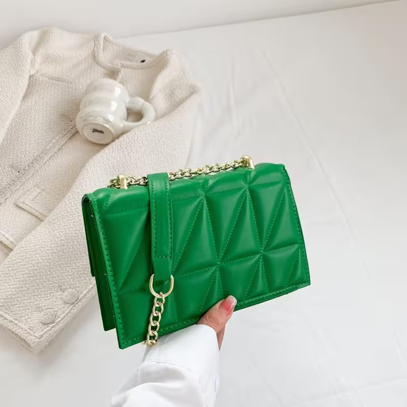 Green quilted handbag with gold chain held by a hand on a white background