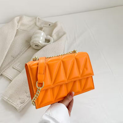 Orange quilted handbag with gold chain held by a hand on a light background