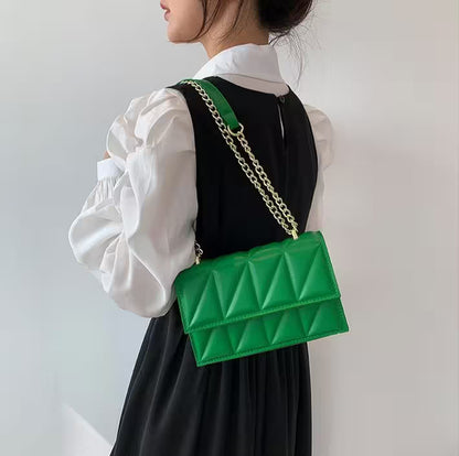 Person wearing a black dress with a white blouse, carrying a green quilted handbag with a gold chain strap.