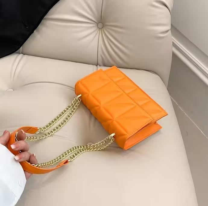 Orange quilted handbag with gold chain strap on a beige couch