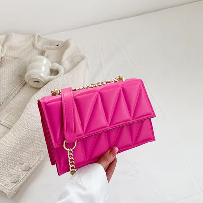 Pink quilted handbag with gold chain held by a hand on a light background
