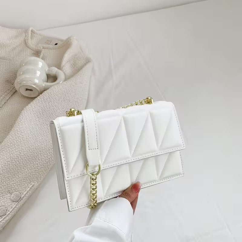 White quilted handbag with gold chain held by a hand on a light gray background