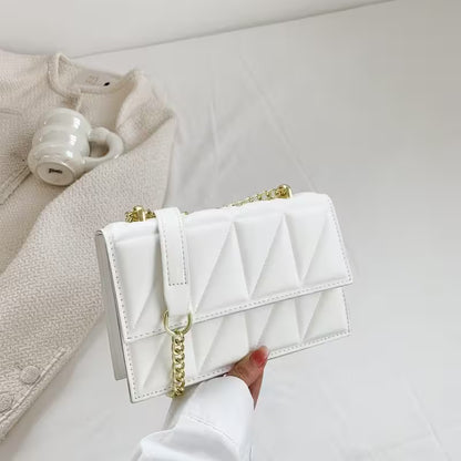 White quilted handbag with gold chain held by a hand on a light gray background