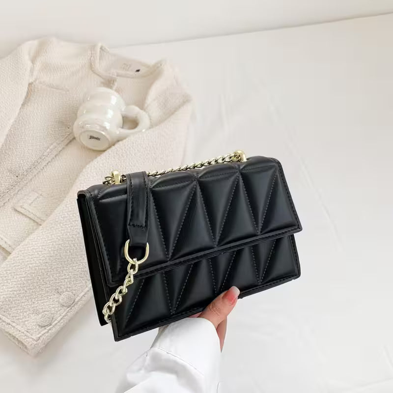 Black quilted handbag with gold chain held by a hand on a light background
