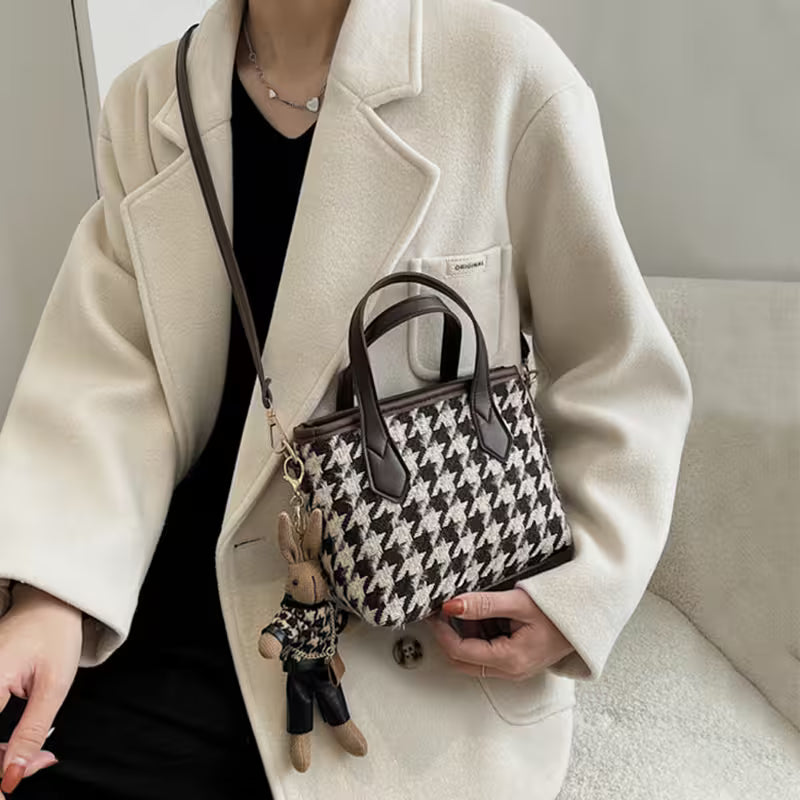 Person holding a patterned handbag with a small plush toy, wearing a beige coat.
