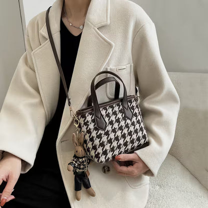 Person holding a patterned handbag with a small plush toy, wearing a beige coat.