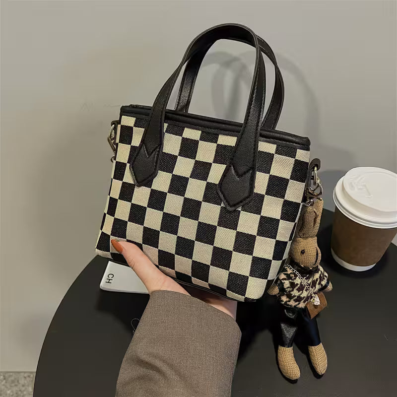 Checkered handbag held by a hand on a table with a coffee cup and small bear toy.