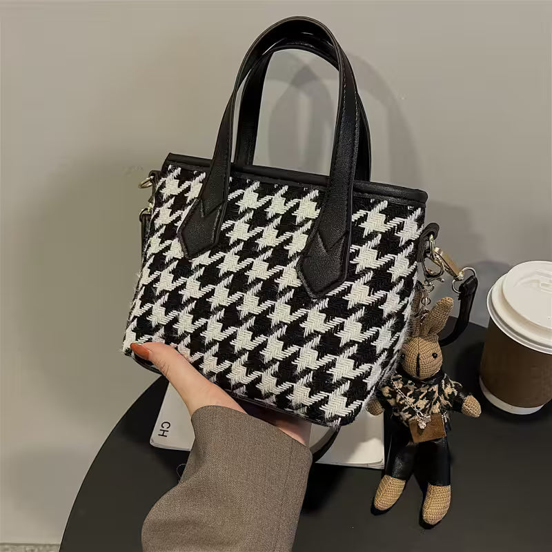 Black and white houndstooth patterned handbag held by a person, with a keychain and coffee cup in the background.
