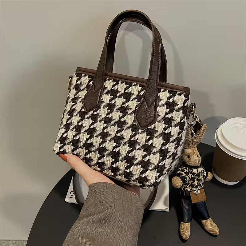 Houndstooth patterned handbag held by a person with a small plush toy and coffee cup in the background.