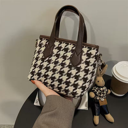 Houndstooth patterned handbag held by a person with a small plush toy and coffee cup in the background.