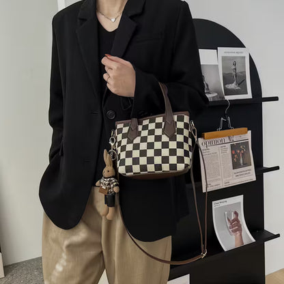Person holding a checkered handbag with a small plush toy, standing in front of a black shelving unit with magazines.