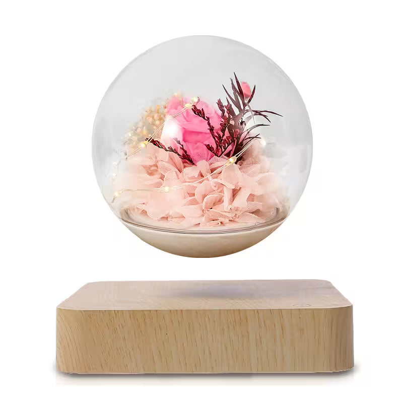 Decorative glass sphere with pink flowers and lights on a wooden base