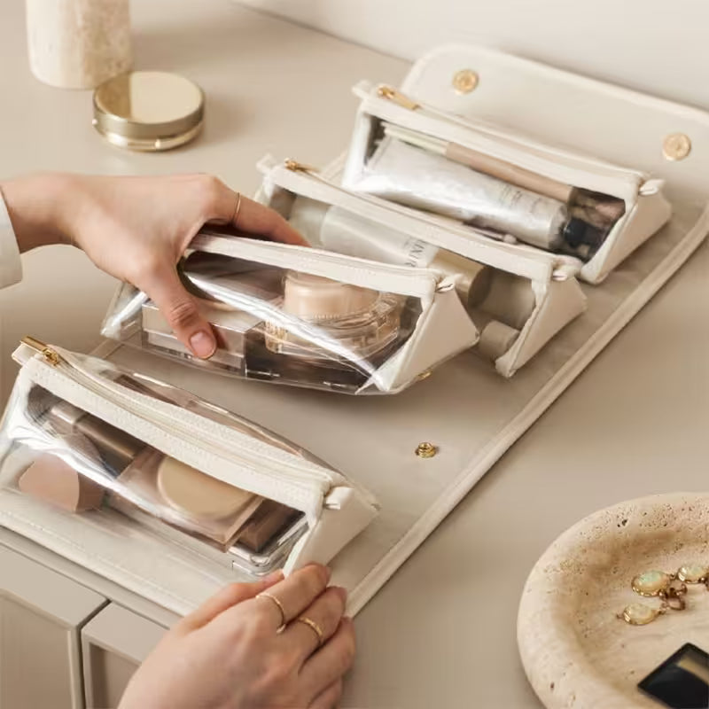 Person organizing makeup items in clear cosmetic bags on a light surface.