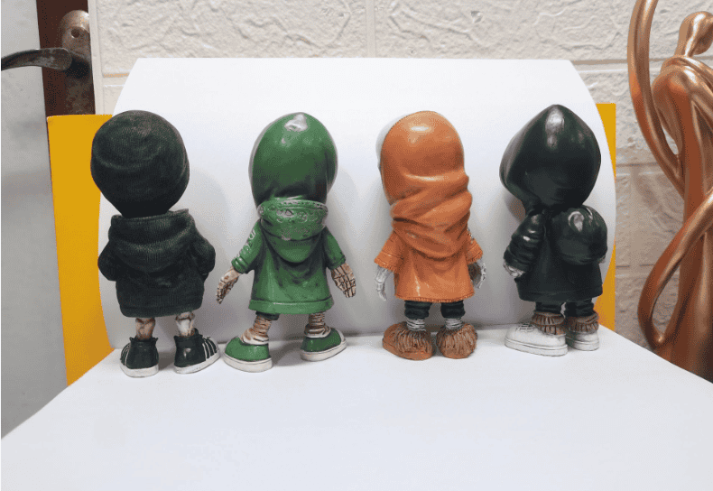 Four bobblehead figures in different outfits on a white surface with a textured wall background.