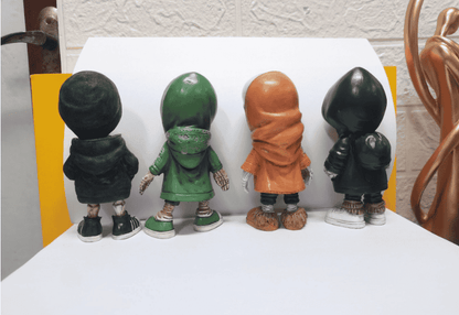 Four bobblehead figures in different outfits on a white surface with a textured wall background.