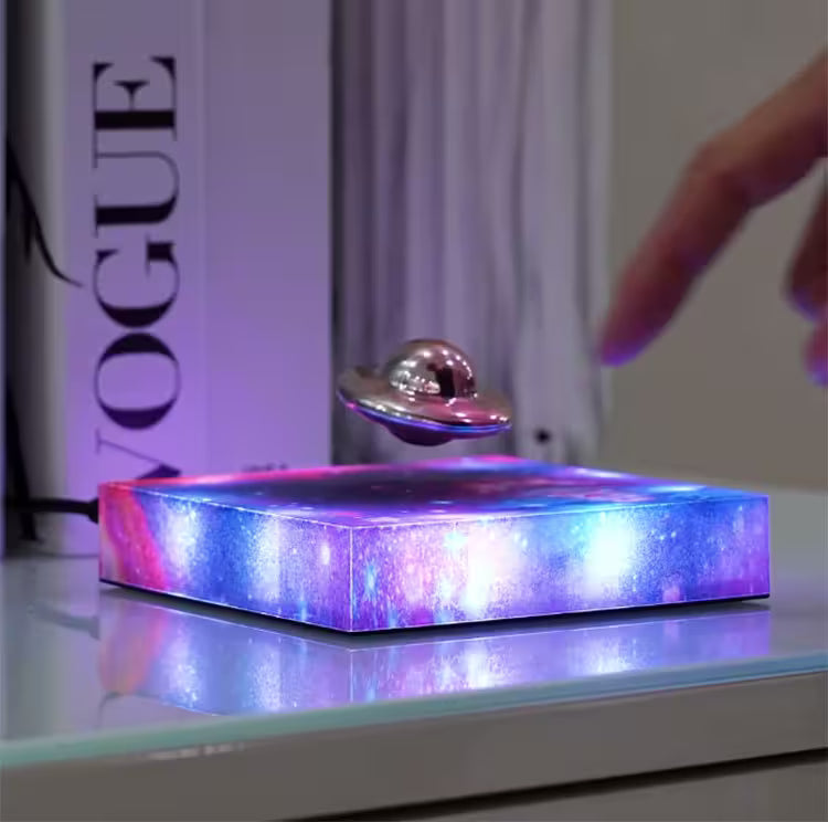 Maglev Levitation Display with colorful base and metallic sphere, placed on a surface with a blurred 'Vogue' magazine in the background.