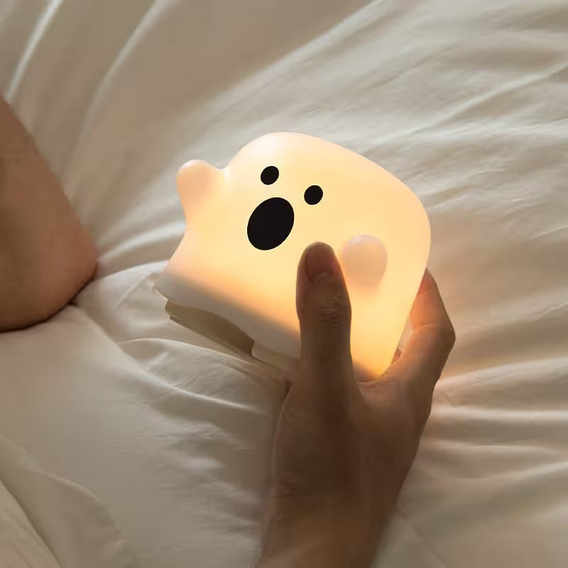 Hand holding a ghost-shaped night light on a bed