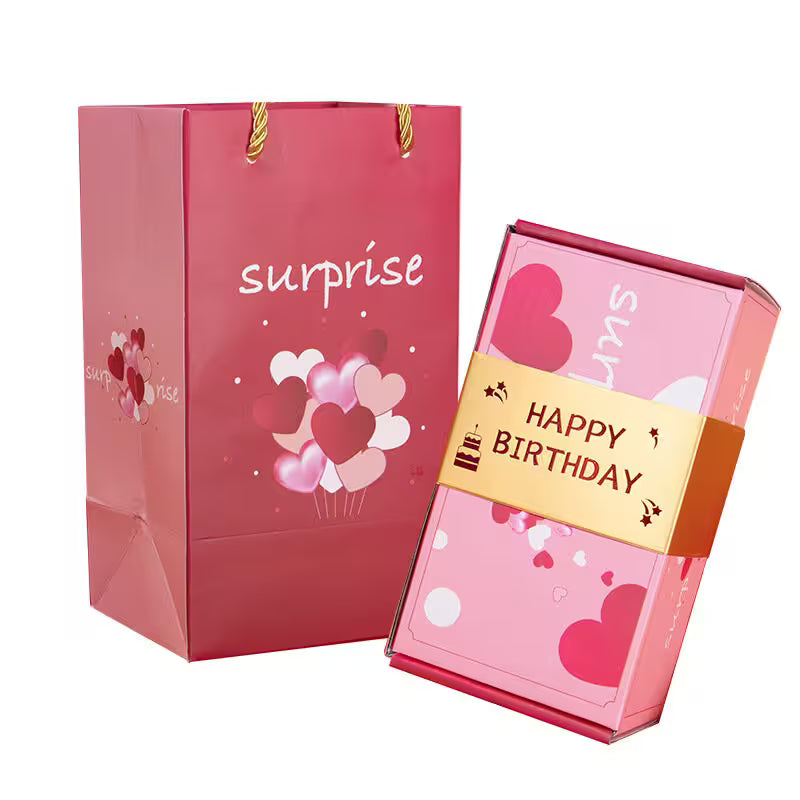 Pink gift bag and box with 'surprise' and 'Happy Birthday' text on a white background