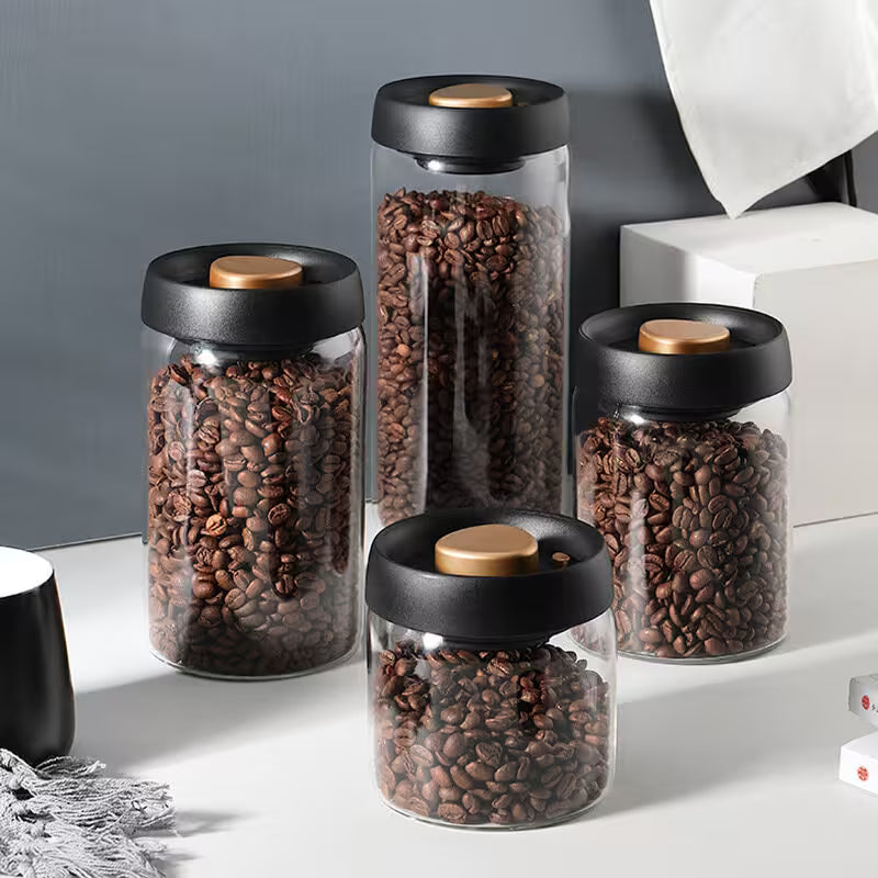 Set of glass jars with black lids and wooden knobs, filled with coffee beans on a light surface.