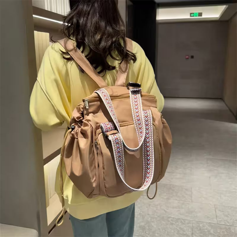 Person holding a brown backpack with decorative straps in an indoor setting