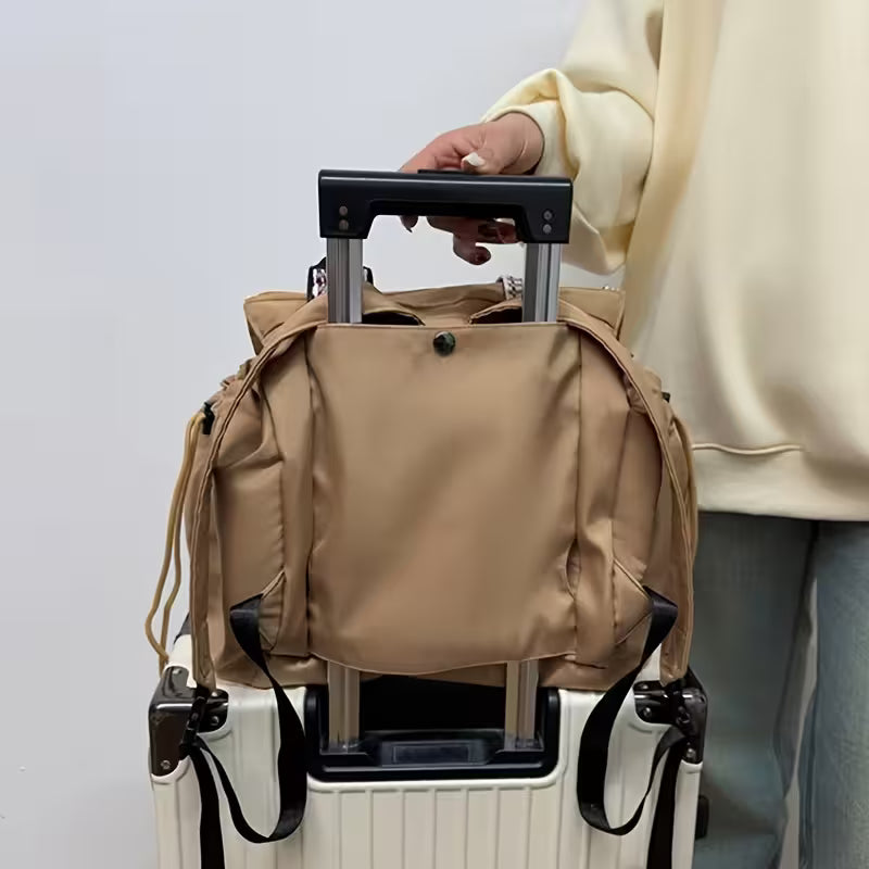 Person holding a beige backpack on top of a white suitcase with a plain background