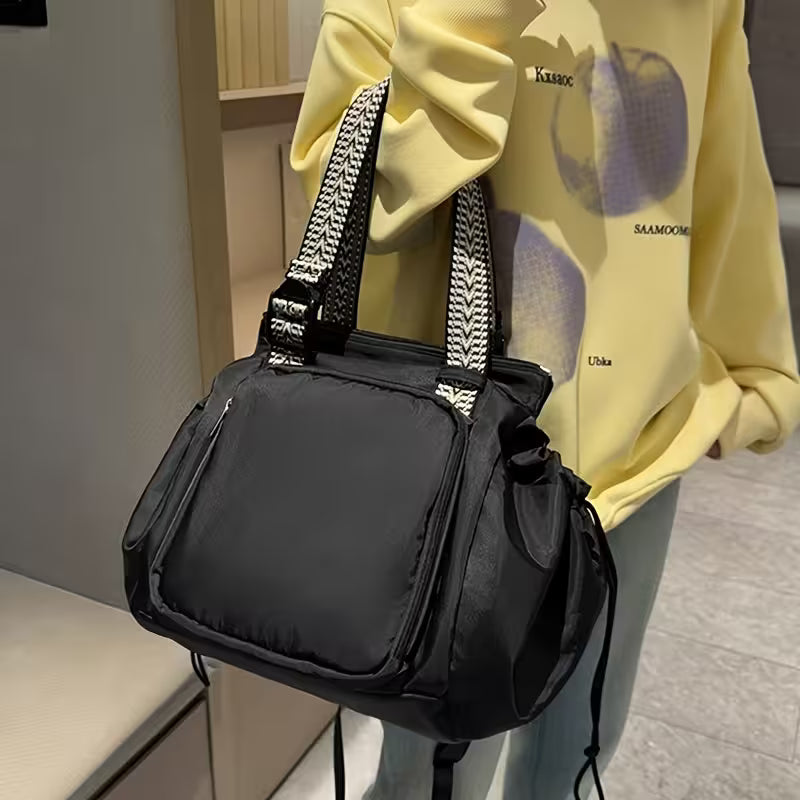 Black handbag with patterned straps held by a person wearing a yellow hoodie.