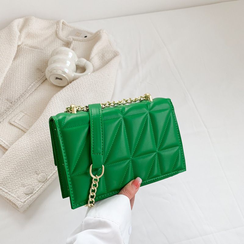 Green quilted handbag with gold chain held by a hand on a light background