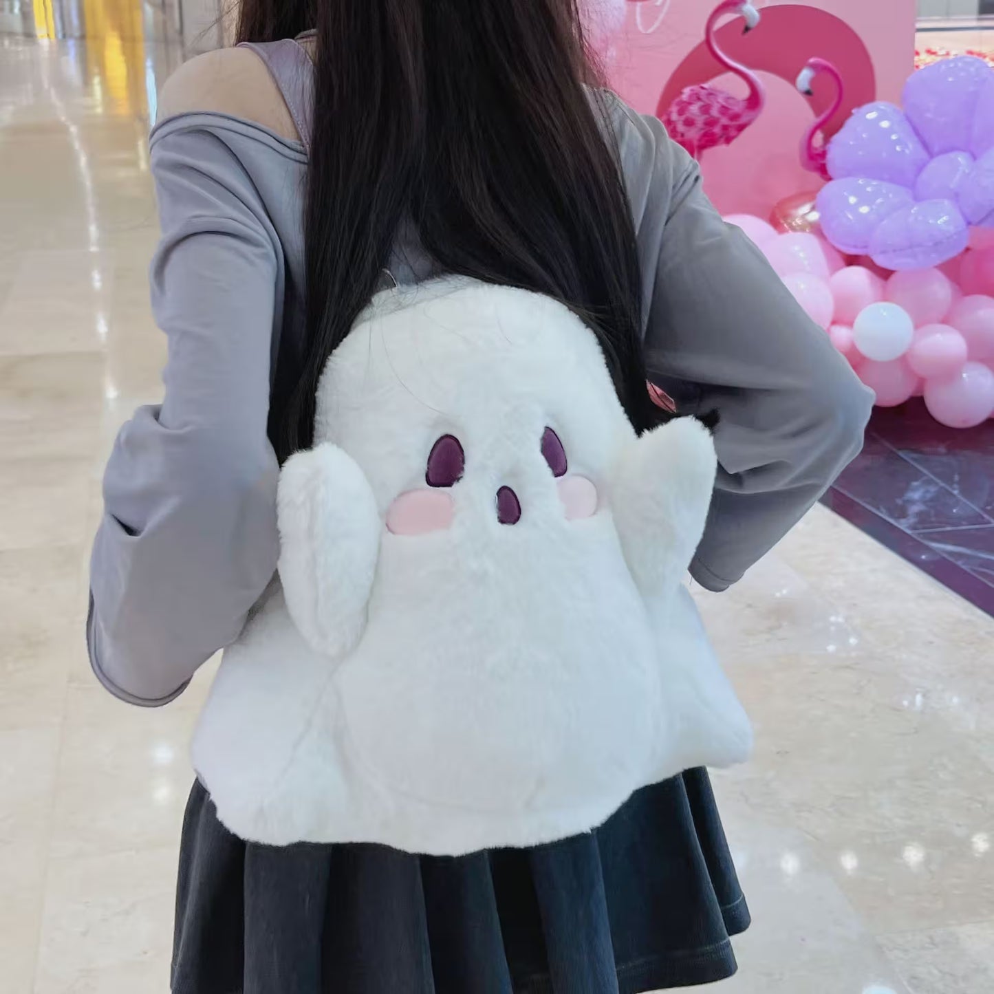 Person wearing a plush ghost backpack in a store setting with balloons and a pink flamingo decoration.