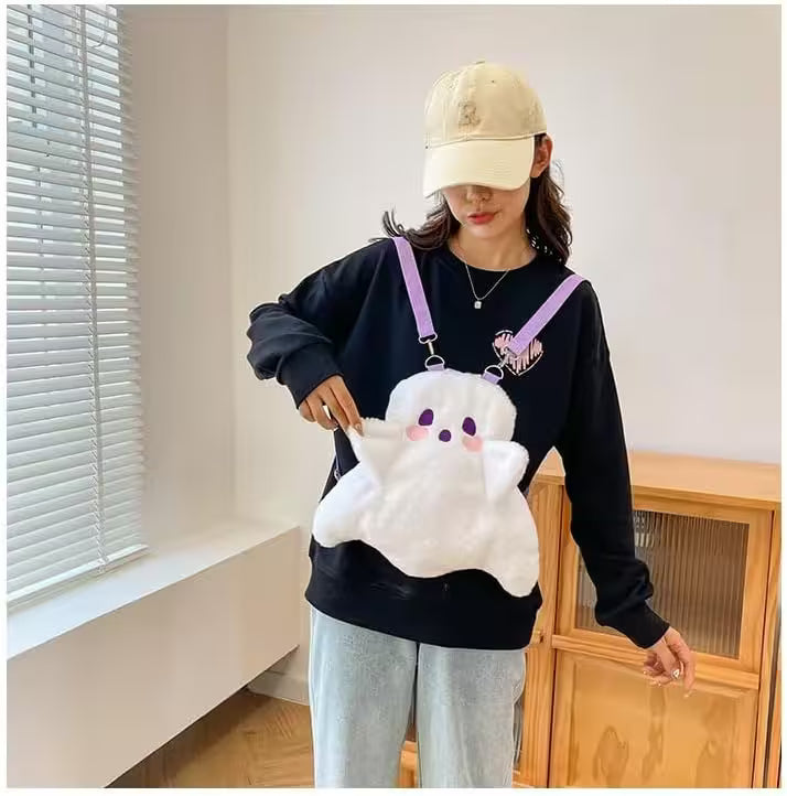 Person holding a plush ghost toy in a room with a window and wooden cabinet.