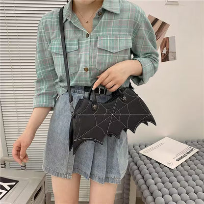 Person wearing a green plaid shirt and denim shorts holding a black bat-shaped purse.