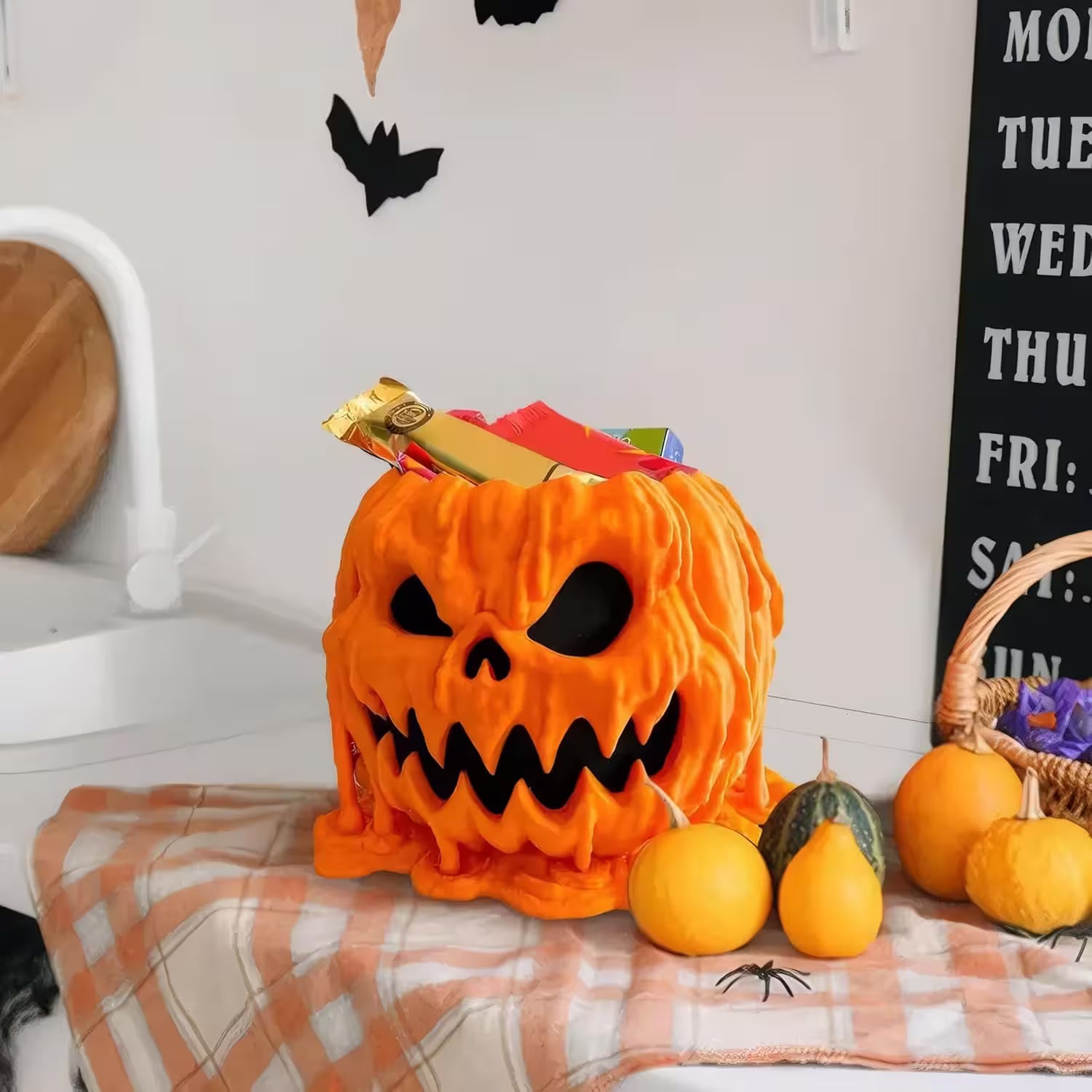 Halloween-themed plush toy resembling a jack-o'-lantern on a checkered blanket with pumpkins around.
