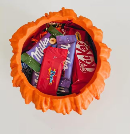 Orange candy dish with various candy bars including KitKat, Milka, and Dubble Bubble on a white background.