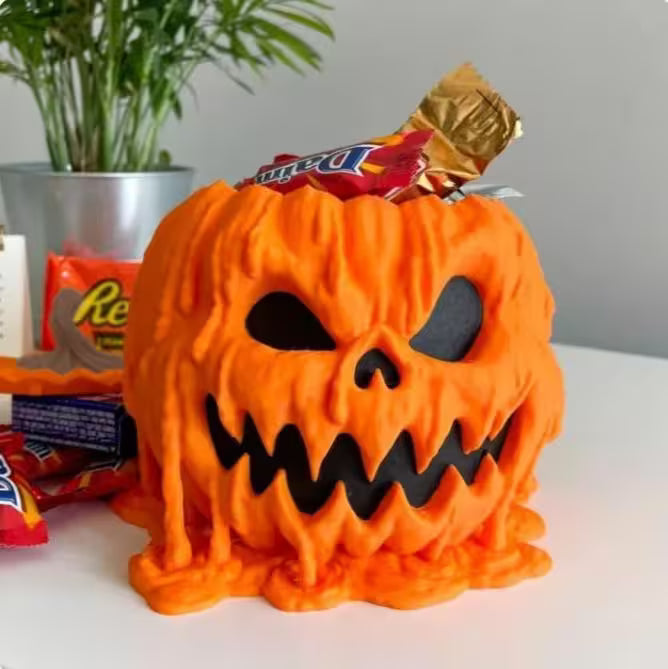 Halloween candy container with a jack-o'-lantern design filled with candy on a white surface.