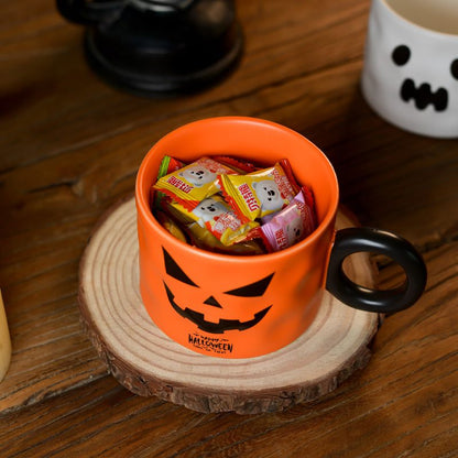 Halloween-themed orange mug with black handle filled with candy on a wooden surface.