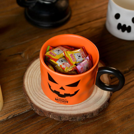 Halloween-themed orange mug with black handle filled with candy on a wooden surface.